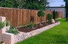A garden scene with a bamboo fence, stone wall, and plants. Anteprima dell’immagine prodotto