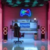 A gaming setup with a neon gamepad sign, gaming chair, computer, and speakers. Produktbild-Vorschau