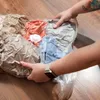 Hands holding a vacuum-sealed bag of clothes on a wooden floor. Podgląd zdjęcia produktu
