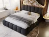 A bedroom scene featuring a dark gray upholstered bed with white and gray bedding. Decorative items are placed on small side tables. Produktbild-Vorschau