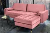 A pink velvet sectional sofa with an ottoman in a modern living room setting. Produktbild-Vorschau