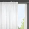 A white sheer curtain hangs in front of a window, partially obscuring the view of green trees and a bright sky outside. Produktbild-Vorschau