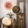 Three paper star lanterns are displayed in a room with rustic decor. One pink lantern hangs on the wall, a green and gold lantern hangs next to it, and a white lantern sits on a chair. Podgląd zdjęcia produktu