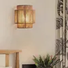 A wall lamp made of jute rope is mounted on a wall next to a curtain and a wooden headboard. Voir les images du produit
