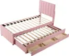 A pink upholstered bed frame with a pull-out trundle bed and storage drawers, shown from a diagonal angle against a white background. Podgląd zdjęcia produktu