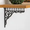 A decorative cast iron shelf bracket is shown mounted on a white wall, supporting a wooden shelf. Podgląd zdjęcia produktu