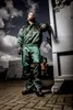 A man in work clothes leans against a large industrial container, with trucks and a cloudy sky in the background. Produktbild-Vorschau