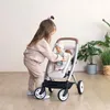 A young girl plays with a doll in a stroller indoors. Produktbild-Vorschau