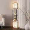 A floor lamp with shelves is placed next to a white sofa and a vase with branches. Produktbild-Vorschau