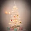 A white artificial Christmas tree decorated with lights and a few ornaments, surrounded by wrapped gifts, with candles in the background. Produktbild-Vorschau