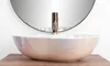 A close-up shot of a pearlescent vessel sink with a gold faucet, set against a white background and a circular mirror. Náhľad obrázku produktu