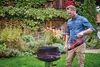 A man is using a red leaf blower to clear out a barbecue grill in a garden. Produktbild-Vorschau