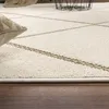 A close-up view of a cream-colored rug with a geometric pattern and a brown woven border, resting on a wooden floor. Anteprima dell’immagine prodotto
