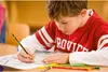 A young boy is drawing with a pencil on a piece of paper, with colored pencils in front of him. Voir les images du produit