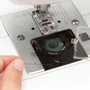 A close-up view of a sewing machine's bobbin area, with a hand holding thread. Produktbild-Vorschau
