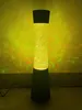 A tall, black lava lamp with a yellow, glittery liquid column is lit up, casting colorful light patterns on a yellow wall. Anteprima dell’immagine prodotto
