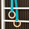 A close-up view of two wooden rings hanging from blue straps, attached to a white bar, against a dark brown ribbed background. Voir les images du produit
