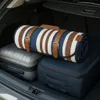 The image shows a rolled-up picnic blanket with brown leather straps and buckles, placed on top of two suitcases in the trunk of a car. Anteprima dell’immagine prodotto