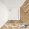 A square shower tray with a drain and a flexible pipe on a wooden floor. Produktbild-Vorschau