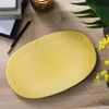 A yellow oval plate is placed on a wooden surface, surrounded by office supplies and plants. Náhľad obrázku produktu