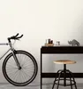 A bicycle is parked next to a desk with decorative items and a stool in front of it. Produktbild-Vorschau