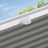 A close-up view of a gray pleated blind attached to a white window frame, with a clear plastic clip holding it in place. The background shows a blue sky with some trees. Produktbild-Vorschau