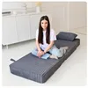 A young woman sits cross-legged on a folded gray mattress in a bright, minimalist room. Voir les images du produit