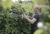 A man is trimming a hedge with an electric hedge trimmer. Produktbild-Vorschau