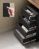 Close up of a black filing cabinet with drawers partially open, showing office supplies, files, and a hand holding a key. Produktbild-Vorschau