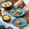 A person is using cutlery to eat a meal served on blue-green speckled plates, with various dishes including a salad, a main course, and a dessert. Voir les images du produit