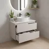 A modern bathroom vanity with two drawers, one open, showcasing its interior. A round sink and black faucet are on top. Plants and decorative items are placed on the vanity and a shelf. Produktbild-Vorschau