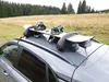A car with a snowboard rack on top, loaded with snowboards and helmets, parked in a grassy, wooded area. Produktbild-Vorschau