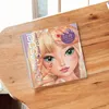 A spiral-bound notebook with a cartoon illustration of a girl's face and hands, decorated with nail stickers, is placed on a wooden table. Anteprima dell’immagine prodotto