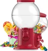 Two red gumball machines with clear globes filled with candy, surrounded by lollipops and loose candies. Náhled obrázku produktu