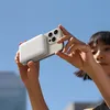 A person is holding a smartphone with a power bank attached to the back, against a clear blue sky. Podgląd zdjęcia produktu