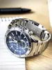 A close-up shot of a silver and blue Casio Edifice watch on a wooden surface, next to a notebook and pen. Podgląd zdjęcia produktu