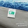Close-up view of the underside of a blue rug, showing the anti-slip backing and a label with product information and certifications. Anteprima dell’immagine prodotto