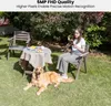 A woman reads a book in a garden next to a dog, with a table and chairs nearby. Produktbild-Vorschau