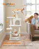 A man is sitting on a couch next to a cat tree with three cats on it. The cat tree is cream white and has multiple levels, a hammock, and scratching posts. There are also orange balls hanging from the cat tree. Produktbild-Vorschau