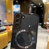 Close-up of the back of a black smartphone case with a silver magnetic ring and camera protection. The background shows a blurred interior of a store or cafe. Náhled obrázku produktu