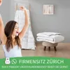 A woman is stretching with her arms up in a bedroom setting, with a folded duvet on a stool in the background. Produktbild-Vorschau