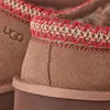 Close-up of the top edge of two brown UGG slippers, showing the decorative stitching and the UGG logo on one slipper. Produktbild-Vorschau