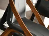 Close-up of a modern dining chair with a black leather seat and curved walnut wood frame. Voir les images du produit