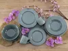 A set of grey porcelain dishes and mugs arranged on a wooden surface with decorative flowers. Náhľad obrázku produktu