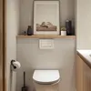 A bathroom scene with a toilet, toilet paper holder, and a shelf with decorative items. Náhľad obrázku produktu