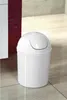 A white plastic trash can with a flip-top lid sits on a tiled floor next to a cabinet. Náhled obrázku produktu