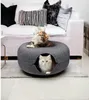 Two cats are in and on a round, dark gray cat bed placed on a rug in a living room setting with a sofa in the background. Produktbild-Vorschau