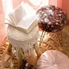 A cozy corner with a book on a macrame stool, a floral ottoman, and a round cushion on a jute rug. Anteprima dell’immagine prodotto