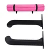 A pink yoga mat rolled up and secured with black straps, shown above two black wall-mounted holders. Podgląd zdjęcia produktu