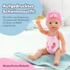A baby doll wearing a pink swimsuit and swim cap sits on a blue towel. Produktbild-Vorschau